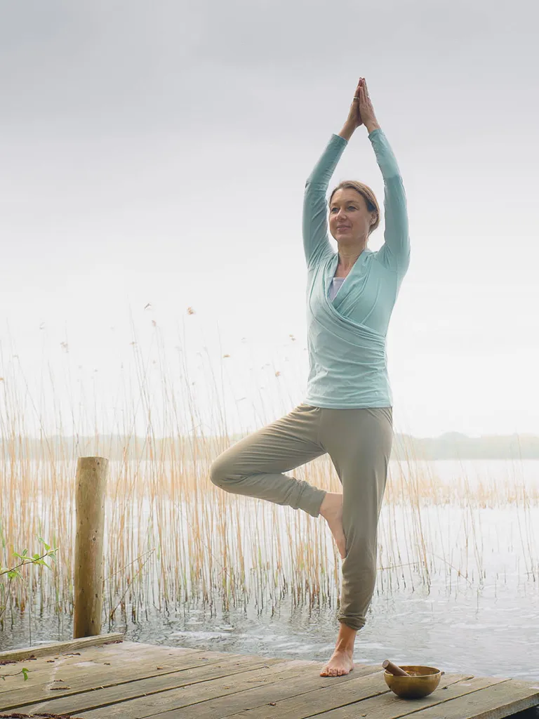 Frau macht Yoga auf einem Holzsteg am See